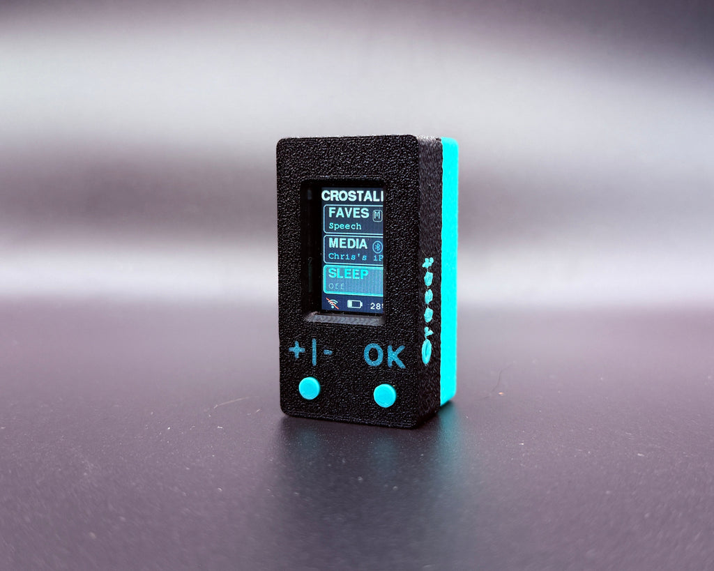 CROSTALK front three-quarter view showing the screen, the plus/minus and OK buttons, and the reset button on the side
