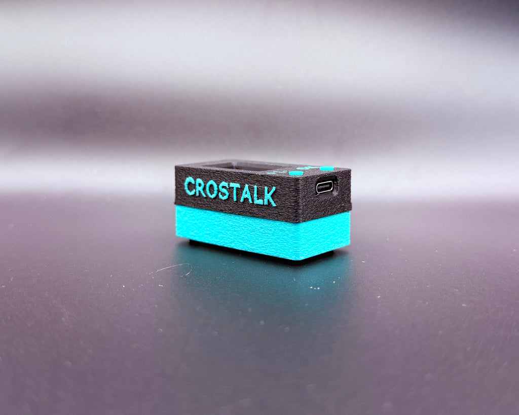 CROSTALK lying flat, showing the raised teal CROSTALK lettering and the USB-C charging port